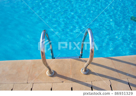 Close up of swimming pool stainless steel handrail descending into tortoise clear pool water. Accessibility of recreational activities concept. 86931329