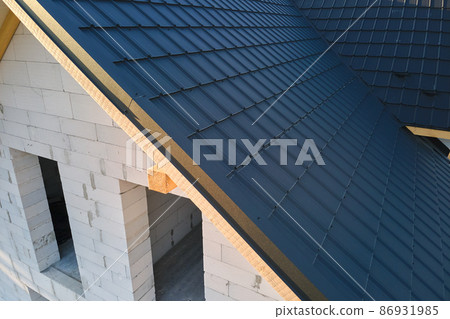 Aerial view of unfinished house with aerated lightweight concrete walls and wooden roof frame covered with metallic tiles under construction. 86931985