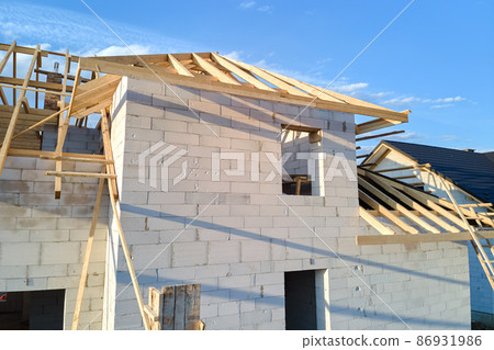 Aerial view of unfinished frame of private house with aerated lightweight concrete walls and wooden roof frame under construction. 86931986