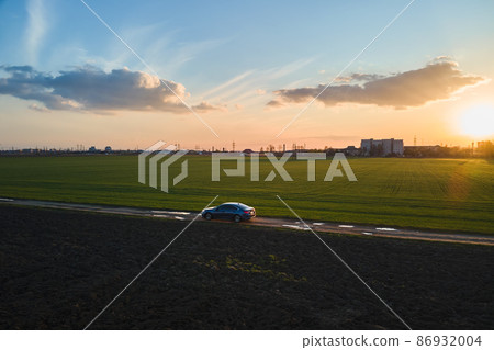 Aerial view of sedan car driving fast on dirt road at sunset. Traveling by vehicle concept. Aerial view of sedan car driving fast on dirt road at sunset. Traveling by vehicle concept. 86932004