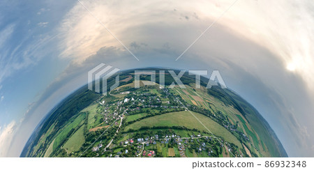 Aerial view from high altitude of little planet earth with small village houses and distant green cultivated agricultural fields with growing crops on bright summer day 86932348