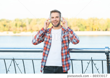happy handsome unshaven man in checkered shirt listen music in headphones outdoor, music happy handsome unshaven man in checkered shirt listen music in headphones outdoor, music 86933017