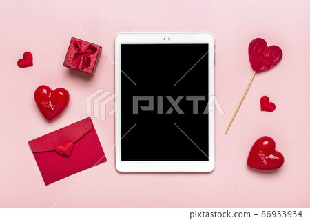 tablet for chooses gifts, makes purchase, envelope, box, two red hearts on pink table Top view Flat lay Holiday shopping list, Happy Valentine's day, party, online shop concept Mock up 86933934