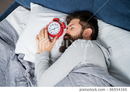 Man sleeping with alarm clock in bed, sleep time 86934160