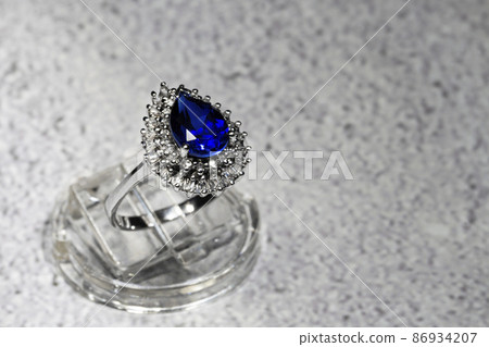 white gold jewelry ring with a large blue pear-cut sapphire and diamonds on a gray background white gold jewelry ring with a large blue pear-cut sapphire and diamonds on a gray background 86934207