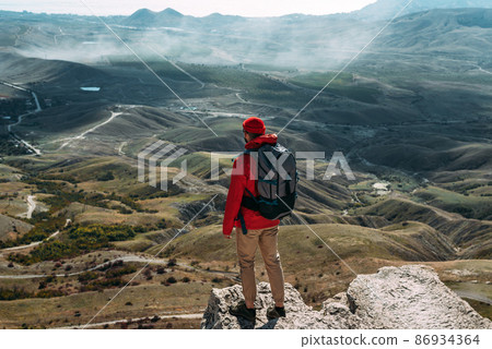 A traveler on the background of mountains. A tourist stands on top of a mountain. Male traveller in the mountains, rear view. Domestic tourism. Copy space A traveler on the background of mountains. A tourist stands on top of a mountain. Male traveller in the mountains, rear view. Domestic tourism. Copy space 86934364
