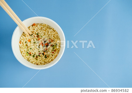 instant noodles with wooden chopsticks on a blue background, top view. Korean national dish. instant noodles with wooden chopsticks on a blue background, top view. Korean national dish. 86934582