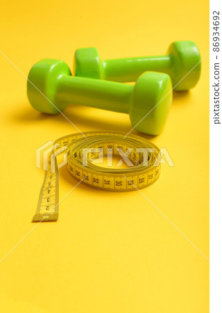 Dumbbells in bright green color isolated on yellow background Dumbbells in bright green color isolated on yellow background 86934692