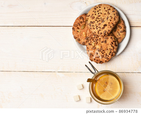 Biscuits with seeds placed near cup of tea and sugar. 86934778