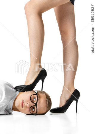 Slender female legs wearing heels pinning young man to floor isolated on white background. Domination, human rights, relationship concept Slender female legs wearing heels pinning young man to floor isolated on white background. Domination, human rights, relationship concept 86935627