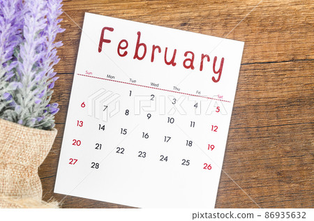 February 2022 calendar with flower on wooden background. 86935632