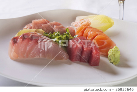 Plate of raw fish sashimi with accompaniment in the foreground 86935646