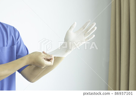 A doctor wearing a blue uniform puts on rubber gloves. in the clinic before treating a patient. A doctor wearing a blue uniform puts on rubber gloves. in the clinic before treating a patient. 86937101