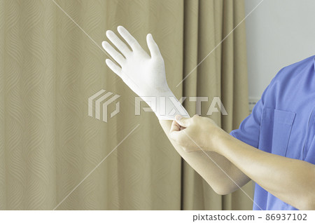 A doctor wearing a blue uniform puts on rubber gloves. in the clinic before treating a patient. 86937102