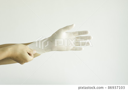 A doctor wearing a blue uniform puts on rubber gloves. in the clinic before treating a patient. A doctor wearing a blue uniform puts on rubber gloves. in the clinic before treating a patient. 86937103