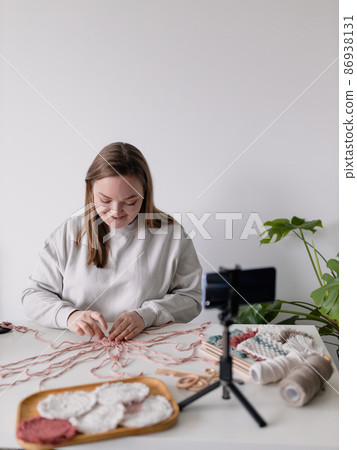 Woman record new videovlog in living room. Puts smartphone on tripod girl make online live stream, lead webinar distant chat, modern tech, video concept. Handmade macrame in work process. Female hobby Woman record new videovlog in living room. Puts smartphone on tripod girl make online live stream, lead webinar distant chat, modern tech, video concept. Handmade macrame in work process. Female hobby 86938131