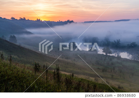 summer morning fog at river behind wild green slope and far forest 86938680