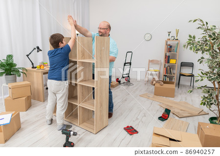 The son and father are happy as they finish assembling the bookcase. The son and father are happy as they finish assembling the bookcase. 86940257