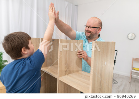 Father and son are happy as they finish assembling the bookcase. Close-up frame. Father and son are happy as they finish assembling the bookcase. Close-up frame. 86940269