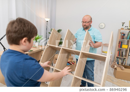 A father and son lift a folding bookcase upright. A father and son lift a folding bookcase upright. 86940296