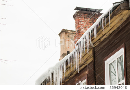 Smooth, transparent icicles hang from the edge of the roof. Smooth, transparent icicles hang from the edge of the roof. 86942048