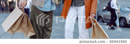 Pair of senior ladies holds shopping bags standing on modern city street Pair of senior ladies holds shopping bags standing on modern city street 86942960