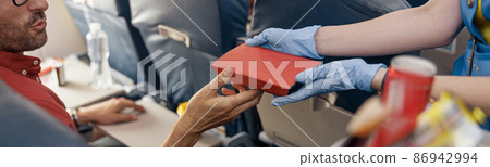 Close up shot of hands of male passenger getting lunch box from female flight attendant serving food on board 86942994