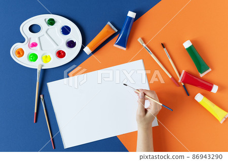 Woman hand painting in sketchbook with pain brush with art supplies around top view on colorful modern. Woman hand painting in sketchbook with pain brush with art supplies around top view on colorful modern. 86943290