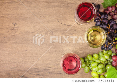 Wine composition with copy space for design. Glasses of red, white and pink wine and variety of grape on wooden background top view. 86943313