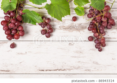 Bunch of ripe red grape with leaves on white wooden background top view. 86943314
