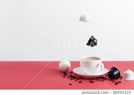 Espresso coffee capsules and roasted coffee beans levitating above coffee cup. Espresso coffee capsules and roasted coffee beans levitating above coffee cup. 86943320