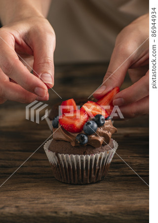 Hands of confectioner decorate cake with fresh berries. Muffin with strawberries and blueberries. Close up cupcake. 86944934