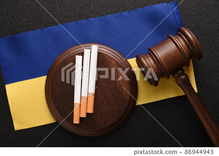 Cigarettes, wooden Judge gavel and flag of Ukraine. Tobacco law. Cigarette smuggling in Ukraine. Tax duties on tobacco products. Cigarettes, wooden Judge gavel and flag of Ukraine. Tobacco law. Cigarette smuggling in Ukraine. Tax duties on tobacco products. 86944943