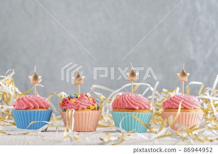 Golden candles in the shape of star on cupcakes. Muffins with pink buttercream frosting on festive tinsel background. Copy spacve on gray wall Golden candles in the shape of star on cupcakes. Muffins with pink buttercream frosting on festive tinsel background. Copy spacve on gray wall 86944952