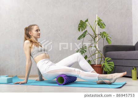 Home workout. Young woman massage thigh muscle with foam massage roller. Equipment for myofascial release Home workout. Young woman massage thigh muscle with foam massage roller. Equipment for myofascial release 86945753