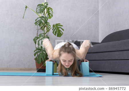 Girl practices yoga using foam blocks. Young woman doing exercise with yoga bricks. Plank pose or chaturanga dandasana 86945772