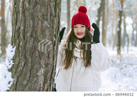 Young beautiful brunette woman in winter in park in bright red hat Young beautiful brunette woman in winter in park in bright red hat 86946032