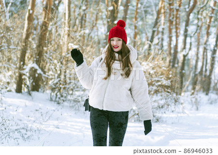 Happy smiling young woman in red hat walks in snowy forest. Sunny day in winter park. 86946033