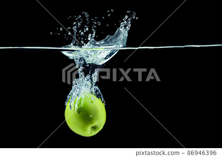 Green apple falling in water with a splash against dark background 86946396