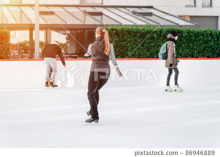 Soft,Selective focus.Outdoor.Winter sport.People, friendship, sport and leisure concept - happy friends on skating rink.Group of teenage friends ice skating on an ice rink. 86946889