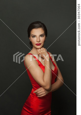 Attractive fashion model woman with makeup wearing red silky dress posing on black background Attractive fashion model woman with makeup wearing red silky dress posing on black background 86947064