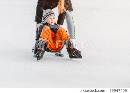 Soft,Selective focus. sport.Mom with baby boy 6 years old, learn train, ride winter city rink, ice skating. The child gets up, fell on skates, kneels, play fun rest on weekend first steps child skates Soft,Selective focus. sport.Mom with baby boy 6 years old, learn train, ride winter city rink, ice skating. The child gets up, fell on skates, kneels, play fun rest on weekend first steps child skates 86947409