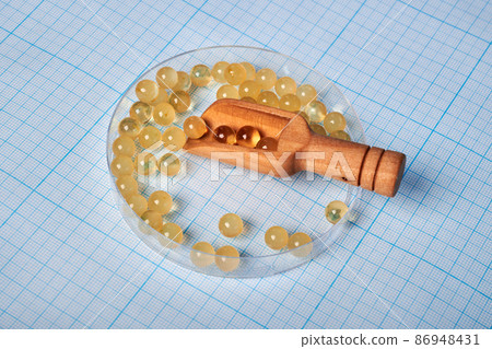 Oil Capsules with Wooden Scoop in Petri Dish - Photo on Graph Paper Oil Capsules with Wooden Scoop in Petri Dish - Photo on Graph Paper 86948431