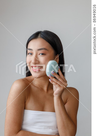 Joyful young woman using face massager in studio Joyful young woman using face massager in studio 86949016