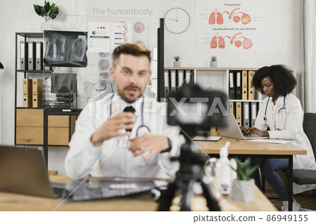 Nurse using laptop while doctor recording video on camera Nurse using laptop while doctor recording video on camera 86949155