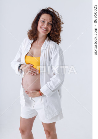 Cheerful pregnant woman in white short standing in studio 86950025