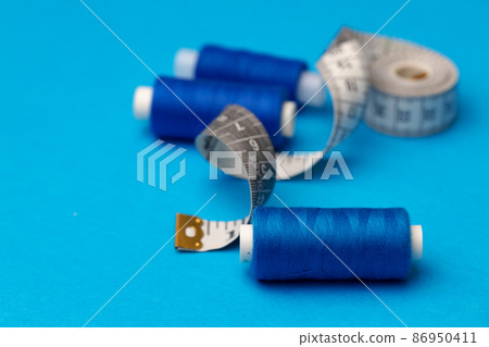 Thread spools and measuring tape on blue background Thread spools and measuring tape on blue background 86950411