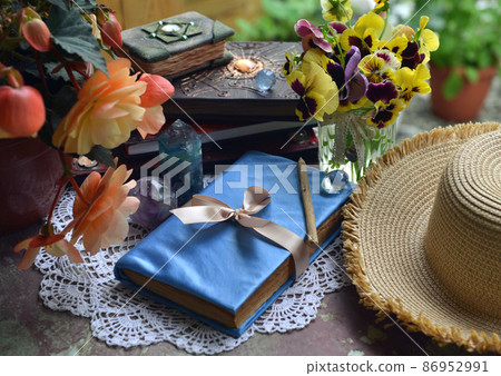Summer still life with old decorated book, crystal stines and beautiful flowers in pots outside in the garden. Vintage background with plants, home hobby still life Summer still life with old decorated book, crystal stines and beautiful flowers in pots outside in the garden. Vintage background with plants, home hobby still life 86952991
