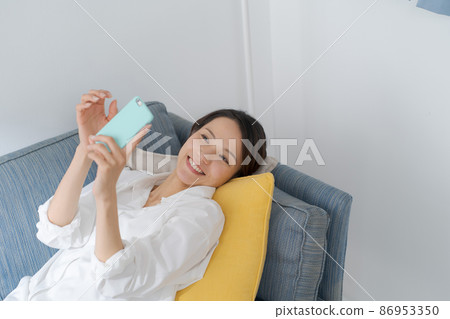 A woman watching a smartphone on a sofa A woman watching a smartphone on a sofa 86953350