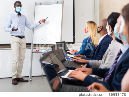 African american businessman in protective mask presenting business project to partners African american businessman in protective mask presenting business project to partners 86955478